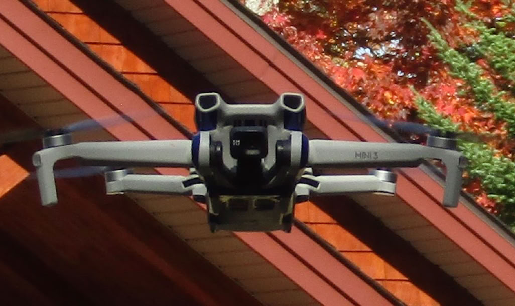 Close-up of a drone in midair with trees in the background, showcasing technology and nature.